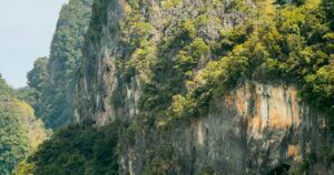 Longtail boat crossing turquoise water before towering limestone cliffs, Phang Nga Bay, Thailand